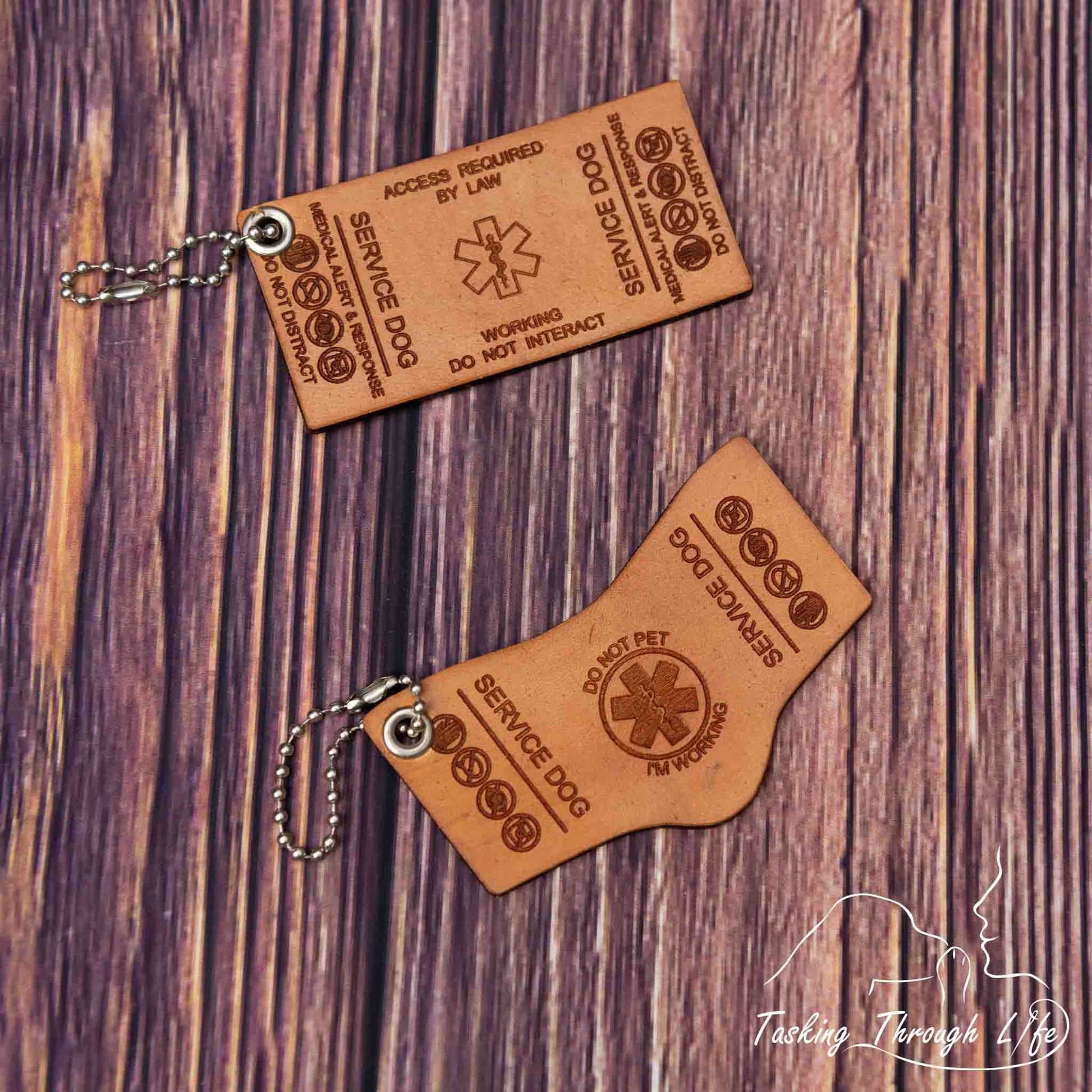 photo showing a close up of 2 laser engraved service dog keychains in various shapes with bead chains, depicting a miniature replica of service dog vest on a wood grain background