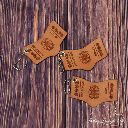 photo showing a close up of 3 laser engraved service dog keychains in the S&R shape with bead chains, depicting a miniature replica of service dog vest on a wood grain background