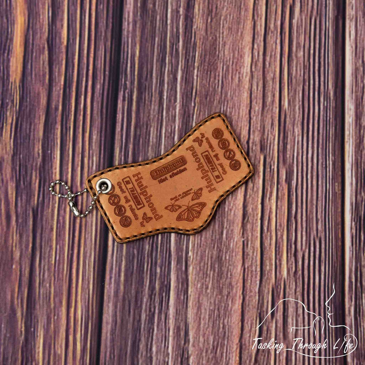 photo showing a close up of a double sided custom laser engraved service dog keychain in the S&R shape, depicting a miniature replica of service dog vest on a wood grain background