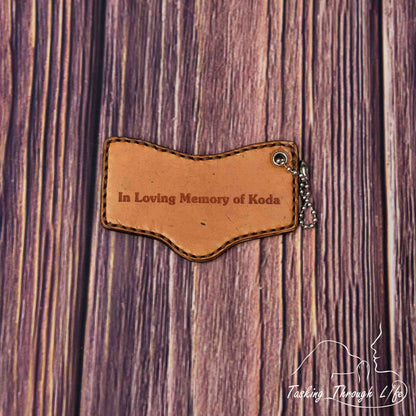 photo showing a close up of the back of a double sided custom laser engraved service dog keychain in the S&R shape, depicting a miniature replica of service dog vest on a wood grain background