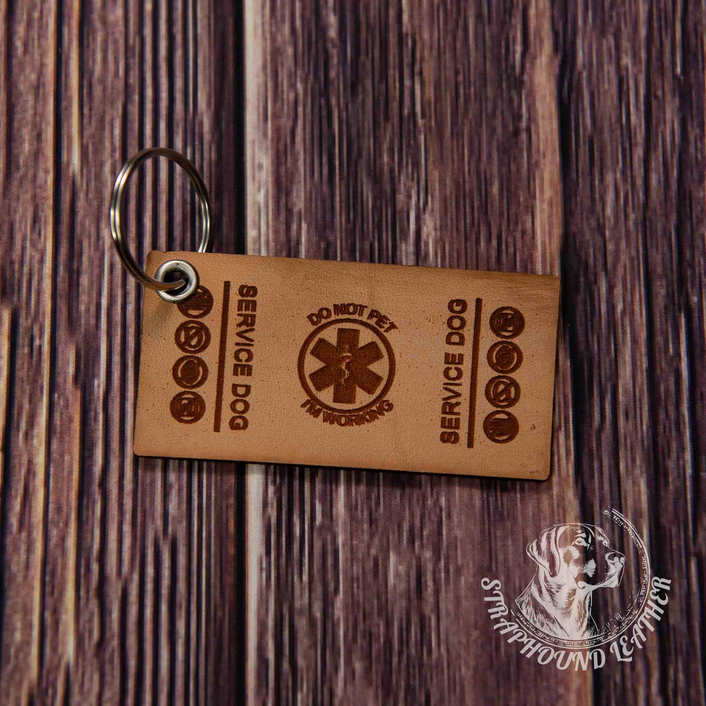 photo showing a close up of a laser engraved service dog keychain in the cape rectangular shape, depicting a miniature replica of service dog vest on a wood grain background