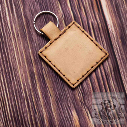 photo showing a square natural leather keychain with a blank side on a wood grain background.